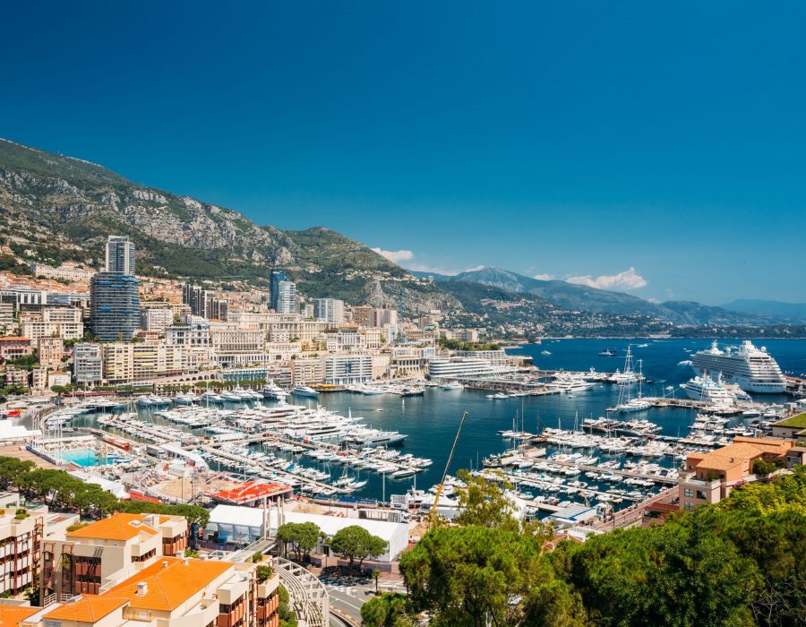 Monaco, Monte Carlo cityscape. Real estate architecture on mountain hill background. Many high-rise buildings in downtown area. Yachts moored at town quay In Sunny Summer Day